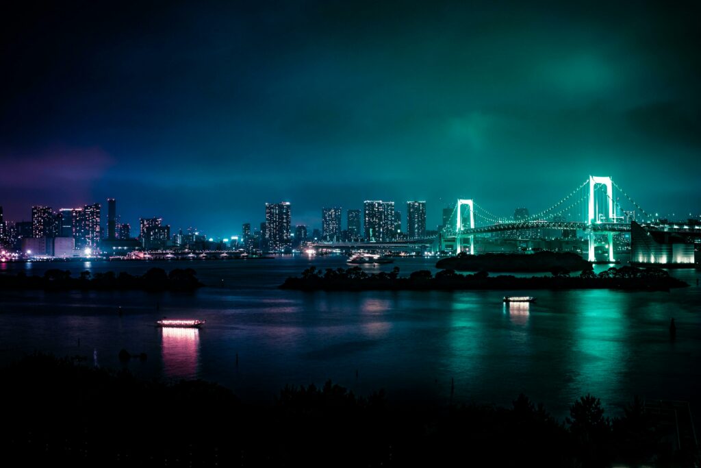Illuminated Tokyo skyline featuring the iconic Rainbow Bridge at night, reflected in calm bay waters.